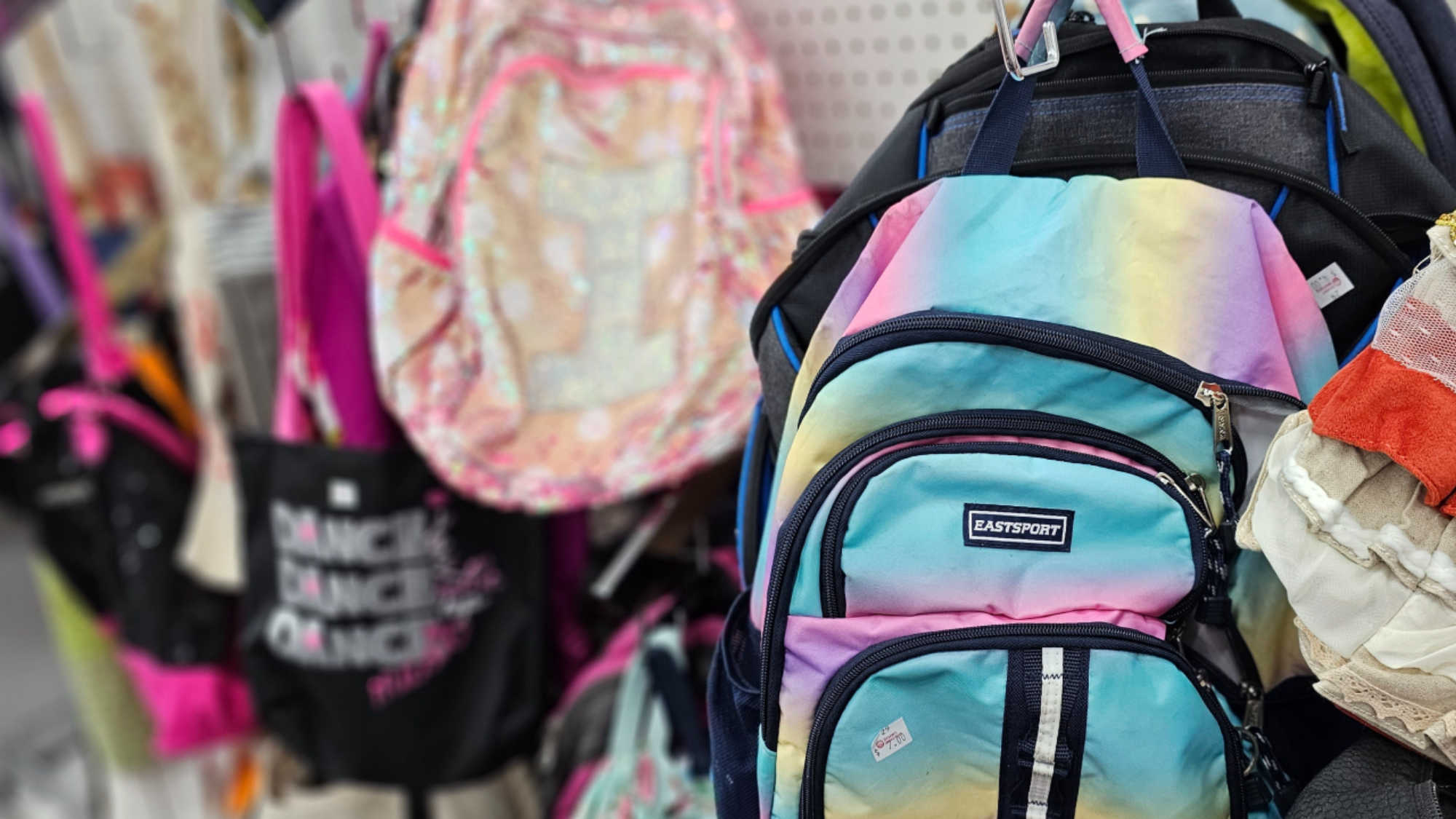 A shelf at Deseret Industries, displaying a row of brightly colored backpacks and totes for students going back to school.